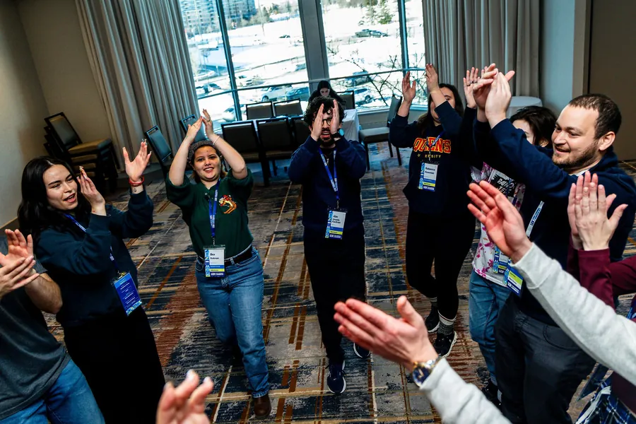 A circle of students clapping together in the hotel conference room.