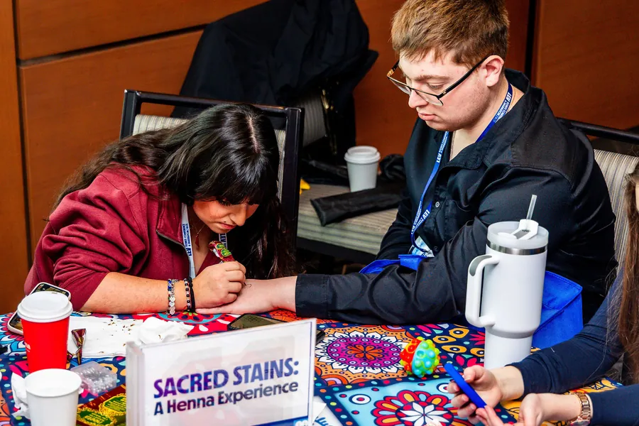 A student drawing henna on another student’s hand.