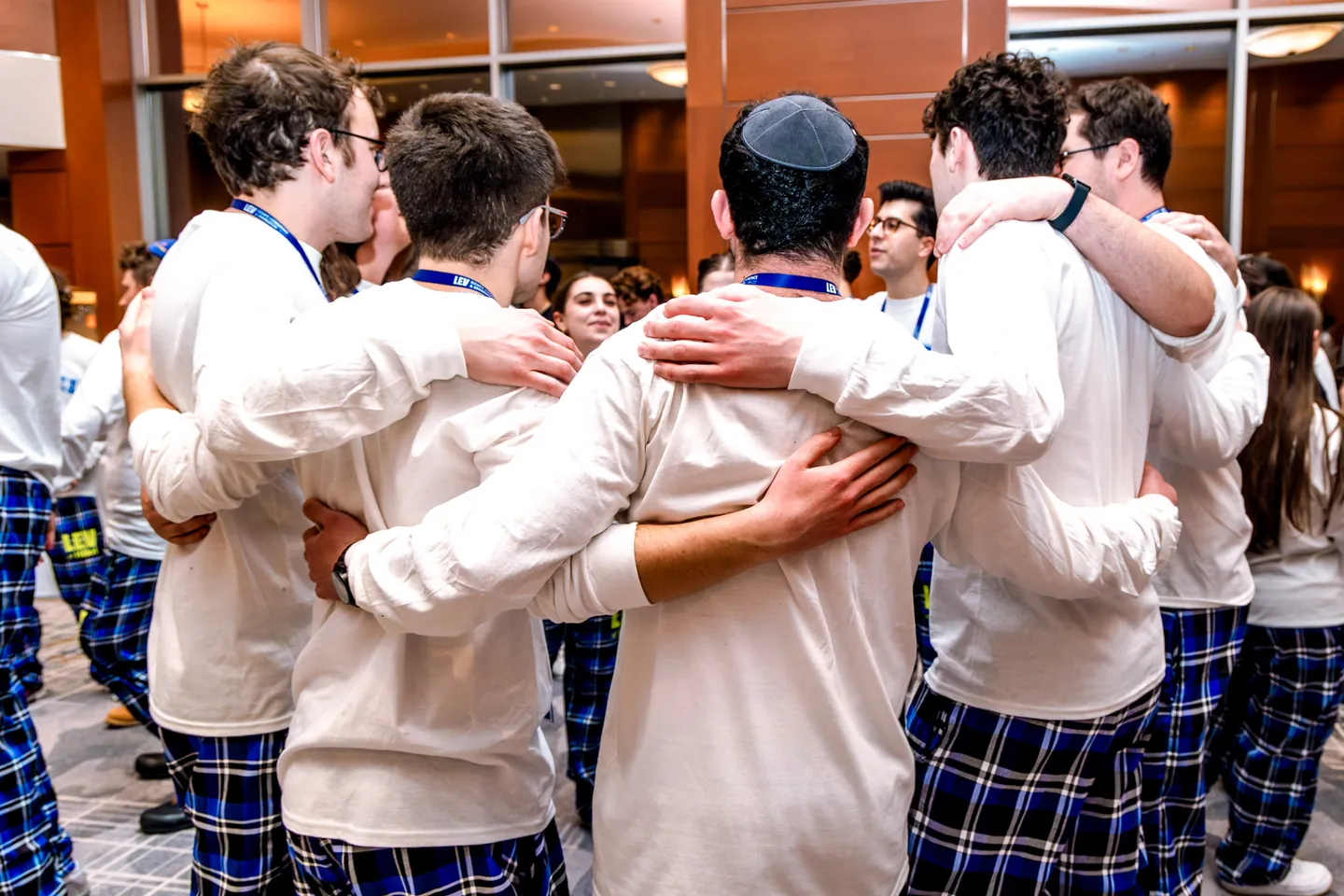 Students seen from behind, standing in a row with their arms around each other.