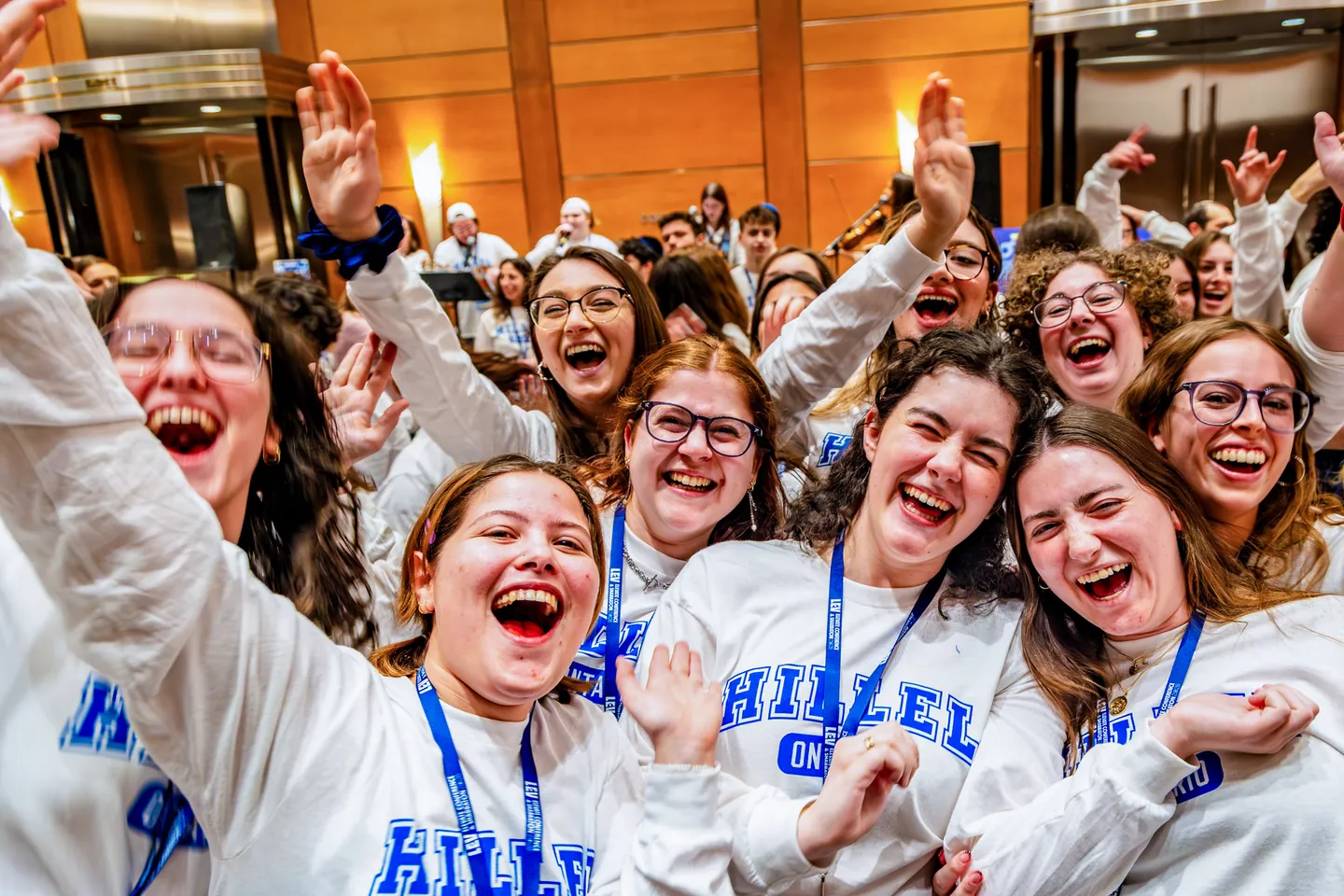 A group of students in Hillel Ontario sweatshirts laughing with their arms in the air.