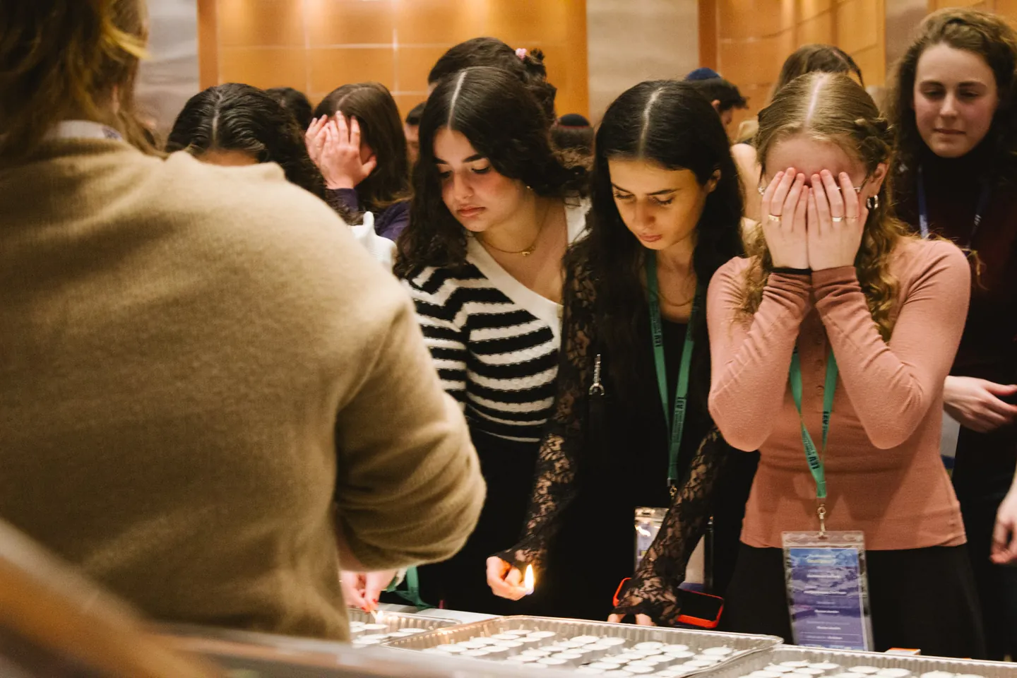 Students lighting Shabbat candles. One covers her eyes.